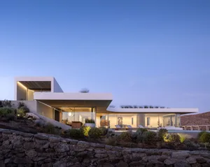 Modern minimalist house exterior with concrete walls, glass windows, and a stone wall surrounding the property.