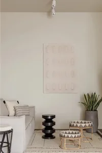 A modern minimalist living room with a white sofa, black and bamboo side tables, and a large potted plant.