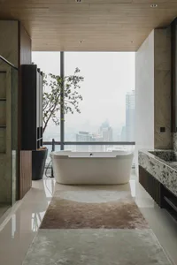 Modern residential bathroom featuring a freestanding bathtub with a cityscape view through large windows and a granite counte