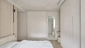 A minimalist bedroom with a concrete wall and floor, featuring light-colored bedding.