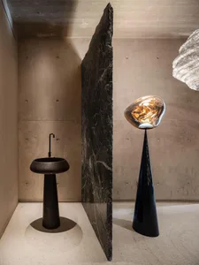A minimalist bedroom with concrete walls and floor, featuring industrial-style furniture and a unique floor lamp.
