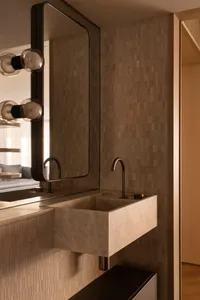 Modern bathroom with a sleek marble sink, illuminated by contemporary wall sconces, against a backdrop of neutral-toned mosai