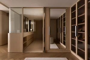 Modern closet featuring wooden cabinetry and glass doors with a bathroom suite in the background.