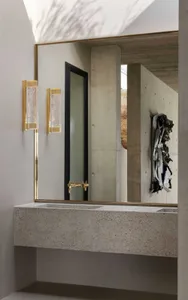 Modern bathroom with concrete vanity, brass faucet, and wall-mounted light fixtures.