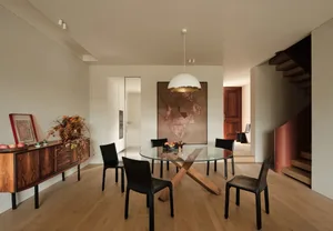 A modern dining room featuring black chairs and a round glass table with wooden legs.