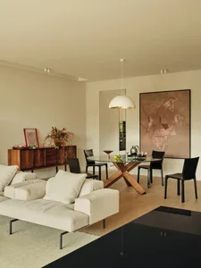 A modern living and dining room featuring a wooden sofa, glass dining table, and black accents on the chairs and floor.