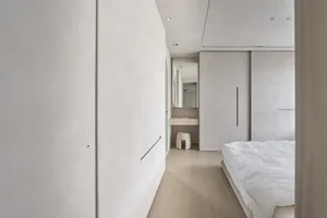 A contemporary minimalist bedroom featuring concrete walls, natural wood flooring, and simple white furniture.