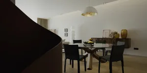 Modern minimalist dining room featuring a round wooden table with glass top and black chairs, illuminated by a minimalist pen