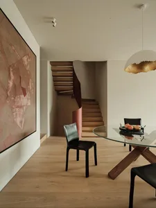A modern minimalist living room featuring wooden stairs, a glass dining table, and black leather chairs.