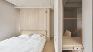 A modern minimalist bedroom with a bed against the wall and a pull-out storage unit.