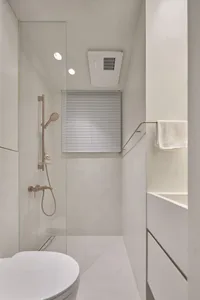 A minimalist, modern bathroom with white concrete walls, a glass shower enclosure, and a sleek design.