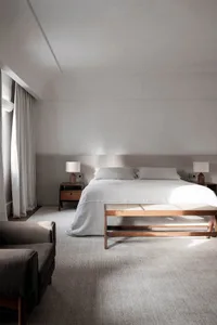 A minimalist bedroom featuring a large bed with linen bedding and wooden furniture.