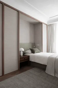 Minimalist bedroom with a bed, side table, and lamp, featuring a wool-blend textile bedspread and headboard.