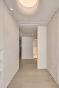 A minimalist corridor with light-colored plaster walls and wooden flooring.