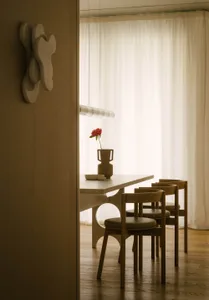 A minimalist dining room with wooden furniture and a single red flower in a vase.