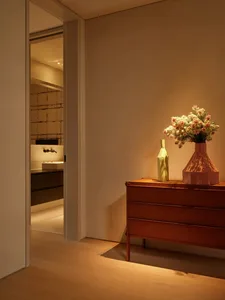 A minimalist entryway featuring wooden furniture and a vase with flowers, illuminated by warm lighting.