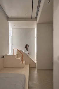 A minimalist interior space featuring wood and concrete elements, with a blurred figure walking down a staircase.