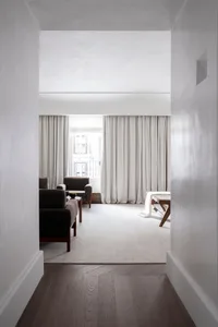 A minimalist living room with dark furniture, a textured carpet, and large windows with white curtains.