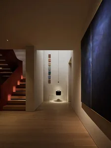 Modern entryway featuring wooden stairs and walls with colorful tiles and a black sculpture on a glass pedestal.