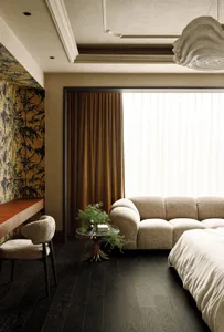 A modern living room featuring a beige upholstered couch with a glass side table holding a plant in a gold vase.