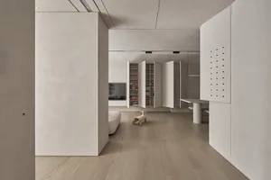A modern living room with light wood flooring, concrete walls, and white furniture.