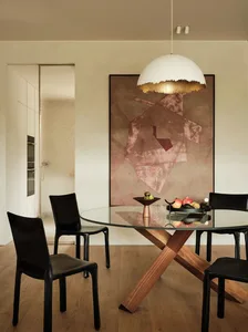 A minimalist dining room featuring a glass table with metal and wood legs, surrounded by black chairs, and a large geometric