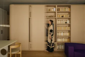 一位人士站在現代簡約圖書館內，木質書架上擺滿書籍，由 XYZ Architects 設計。