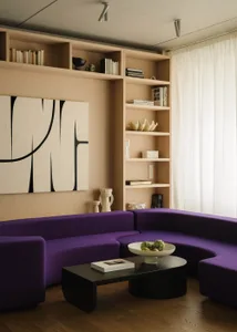 A modern living room featuring a purple curved sofa and a built-in bookshelf with decorative items.