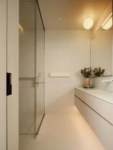 Modern, minimalist white bathroom with glass shower enclosure, white marble sink, white tiled floor, white stainless steel fi