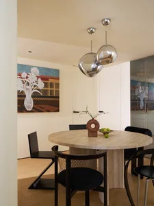 Modern minimalist dining room with a round marble table and black chairs.
