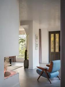 A modern minimalist living room with a concrete floor, blue armchair, and large windows.