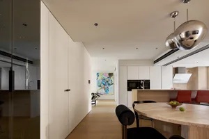 A minimalist residential kitchen with white cabinetry and wooden flooring.