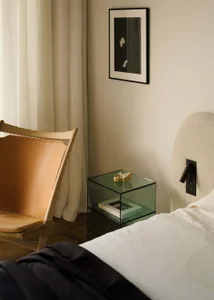 A modern bedroom featuring a glass side table, minimalist bed, and a framed artwork on the wall.