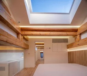 A modern bedroom featuring wooden beams on the ceiling and a skylight allowing natural light to enter the room.