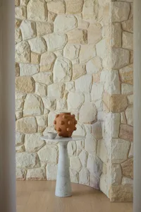 A modern entryway featuring a stone floor and a concrete table with a unique vase on it.