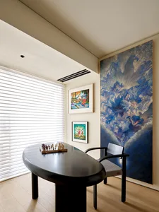 A modern home office featuring a large, abstract painting on the wall, along with a sleek, oval-shaped desk and a comfortable