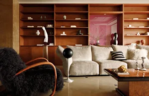 A modern living room with a white sofa, black fur chair, and wooden bookshelves.
