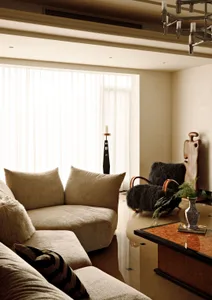 Modern living room with beige sofa, black armchair, wooden table, and marble floor.