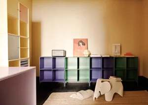 A modern living room featuring colorful metal shelves, a white elephant stool, and a painting of a woman on a beige wall.