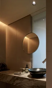 Modern bathroom with round mirror, black sink, and marble countertop.