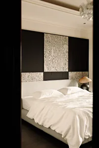 A modern minimalist bedroom featuring a white upholstered bed with a simple headboard, placed against a wall with dark and li