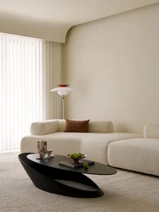 A modern minimalist living room with a white modular sofa and a black sculptural coffee table, featuring a marble vase and gr