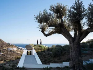 Two people observing the landscape from a modern structure on a hillside overlooking the sea.