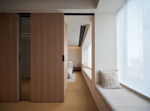A modern bedroom featuring a window seat with cushions, wooden cabinets, and a minimalist window treatment.