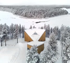 A modern winter cabin covered in snow with a wooden exterior.