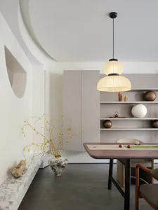 A minimalist dining room featuring a wooden table, marble accents, and a layered light fixture