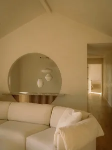 A minimalist white leather living room with a circular mirror and pendant lights.