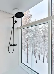 A modern bathroom with black fixtures, a white glass window, and a view of a snowy forest.