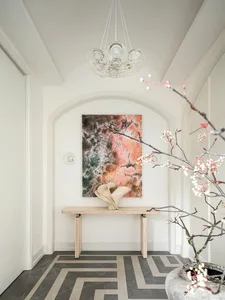 A modern entryway with a minimalist design, featuring a concrete floor and a table with a vase and abstract painting.