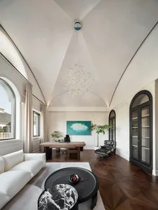 A spacious modern home office with a large white sofa, a black and white marble coffee table, a wooden desk, and a black loun